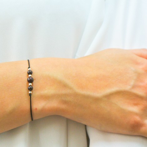 Garnet bead friendship bracelet on thin black cord with small silver details, worn on wrist