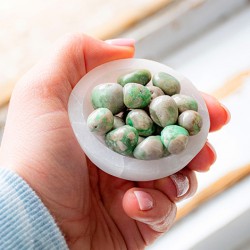 Hand holding a white bowl filled with variscite pocket stones